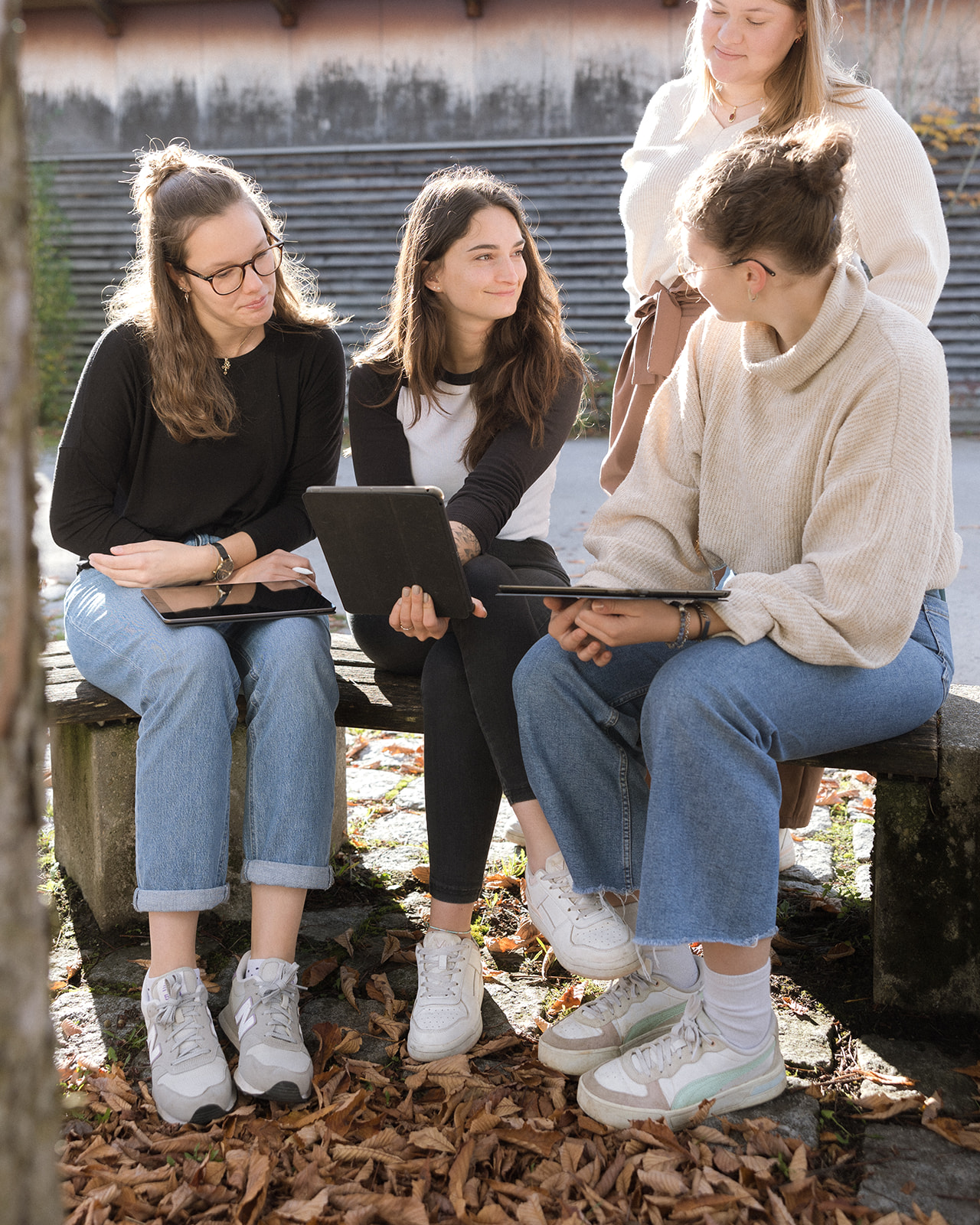 Gemeinsames Lernen und Austausch der Auszubildenden Vier junge Auszubildende der Berufsfachschule Agatharied sitzen im Freien auf einer Bank und unterhalten sich angeregt, teilweise mit Tablets, was den Austausch und das Lernen fördert.